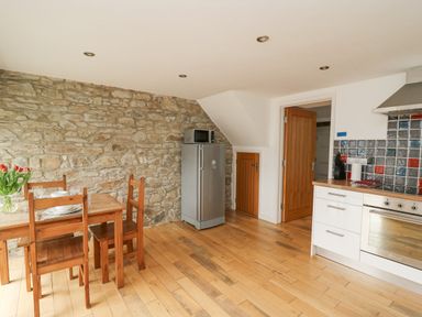 A kitchen with wooden floor table and chairs fridge microwave and oven at Y Cwtch in Newport