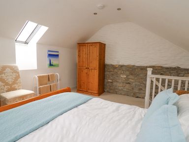A bedroom with a bed, wooden wardrobe, chair, towel rack, and skylight at Y Cwtch in Newport