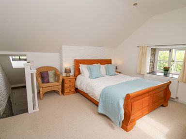 A bedroom with a wooden bed with white and blue bedding a wicker chair and a window with a flower pot at Y Cwtch in Newport