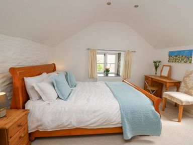 A bedroom with a wooden bed white bedding blue pillows and blanket a wooden nightstand and desk with flowers at Y Cwtch in Newport