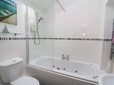 A bathroom with a bathtub shower combination toilet and wall art at Y Cwtch in Newport