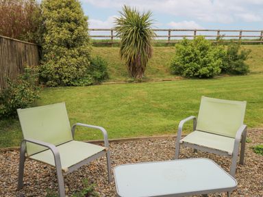 Two outdoor chairs and a table on a gravel area with grass and shrubs in the background at Y Cwtch in Newport