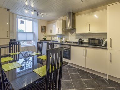 A kitchen with a black dining table and green placemats white cabinets tiled floor and window at The Old Exchange in Corbridge near Hexham