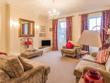 A living room with beige sofas red curtains and a chandelier at The Old Exchange Corbridge near Hexham