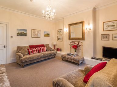 A living room with sofas cushions a chandelier wall art mirror and a television at The Old Exchange in Corbridge near Hexham