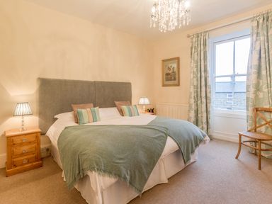 A bedroom with a double bed two bedside tables with lamps a window with curtains and a wooden chair at The Old Exchange in Corbridge near Hexham