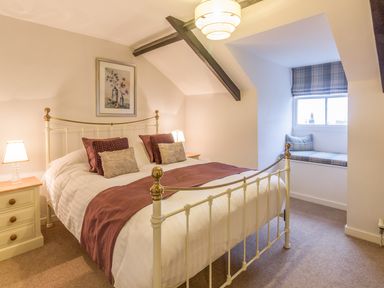 A bedroom with a metal bed frame with pillows and blankets two bedside tables with lamps a window seat with cushions and a framed picture on the wall at The Old Exchange in Corbridge near Hexham