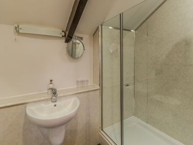 A bathroom with a wall-mounted sink a soap dispenser a small round mirror and a glass enclosed shower at The Old Exchange in Corbridge near Hexham