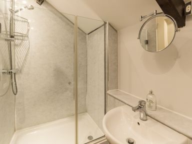 A bathroom with a shower enclosure a sink with a faucet a round wall-mounted mirror and a soap dispenser at The Old Exchange in Corbridge near Hexham