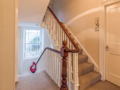 A carpeted staircase with white balusters and dark wooden handrail next to a window with a red decorative object at The Old Exchange in Corbridge near Hexham