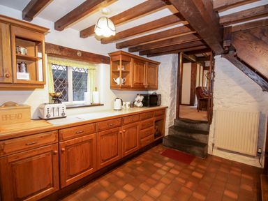 A kitchen with wooden cabinets tiled floor and a cream countertop at Nant Cottage in Llanrwst near Betws-y-Coed