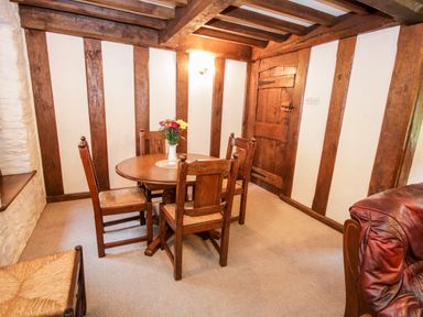 A room with a round wooden table with four chairs and a vase of flowers on the table at Nant Cottage in Llanrwst near Betws-y-Coed