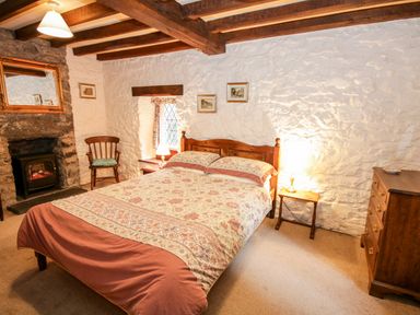 A bedroom with a double bed beside a window and a stone fireplace with a wooden chair and a dresser at Nant Cottage in Llanrwst near Betws-y-Coed