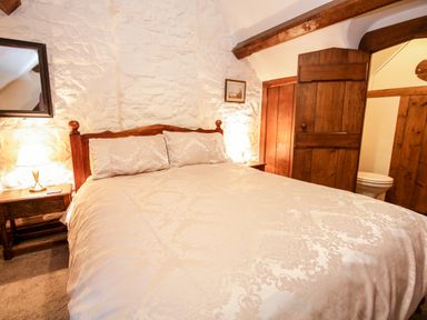 A bedroom with a wooden bed frame bedside tables lamps and a wooden door at Nant Cottage in Llanrwst near Betws-y-Coed