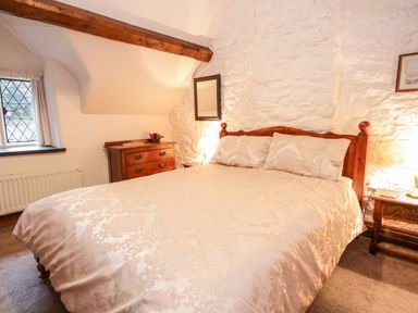 A bedroom with a wooden bed a chest of drawers a bedside table with a lamp and a window at Nant Cottage in Llanrwst near Betws-y-Coed