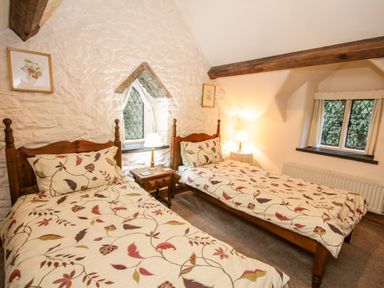 A bedroom with two single wooden beds with floral bedding a wooden bedside table with a lamp two framed pictures and two windows at Nant Cottage in Llanrwst near Betws-y-Coed
