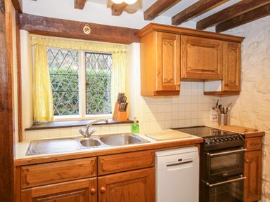A kitchen with wooden cabinets a double sink a dishwasher a black oven and yellow curtains at Nant Cottage in Llanrwst near Betws-y-Coed