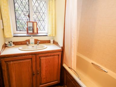 A bathroom with a wooden vanity sink cabinet a bathtub with a shower curtain and a window with yellow curtains at Nant Cottage in Llanrwst near Betws-y-Coed
