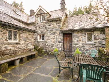 A stone courtyard with wooden and plastic chairs and a table outside a stone cottage Nant Cottage Llanrwst near Betws-y-Coed