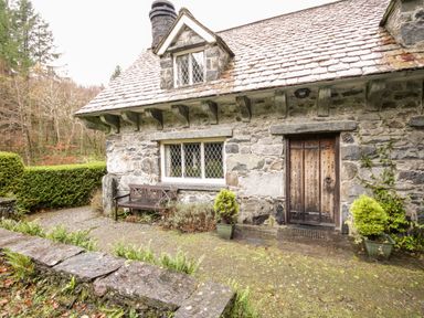 Stone exterior of a cottage with wooden door window bench and plants at Nant Cottage in Llanrwst near Betws-y-Coed