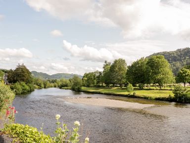 A river flowing through a landscape with trees on both sides and hills in the background at Nant Cottage in Llanrwst near Betws-y-Coed