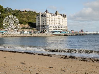 A sandy beach with sea waves in front of a large white hotel building and a Ferris wheel near a pier at a seaside location