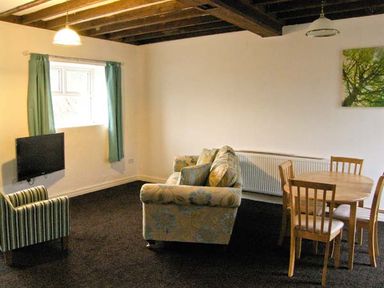 A living room with a striped armchair a sofa a round wooden dining table with chairs and a wall-mounted TV at Hendre Aled Cottage 3 Llansannan