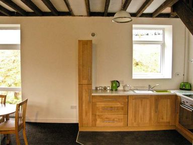 A kitchen with wooden cabinets a dining table with chairs and kitchen appliances at Hendre Aled Cottage 3 in Llansannan