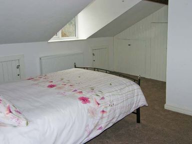 A bedroom with a bed with floral bedding under a slanted ceiling with small white doors at Hendre Aled Cottage 3 in Llansannan