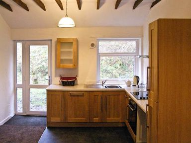 A kitchen with wooden cabinets a door and a window at Hendre Aled Cottage 1 in Llansannan near Llanrwst