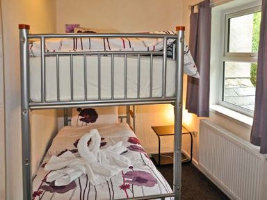 A bedroom with a metal bunk bed and a nightstand near a window with curtains at Hendre Aled Cottage 1 in Llansannan near Llanrwst