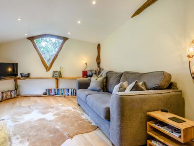 A living room with a gray sofa a wooden side table bookshelves and a triangular window at Brookbank Folly in Mitcheldean
