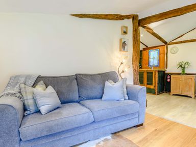 A grey sofa with cushions and a blanket in a living space with wooden beams and a adjacent kitchen area at Brookbank Folly in Mitcheldean