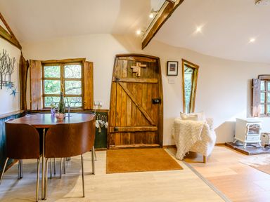 A wood door next to a dining table with chairs a window and an armchair with a throw in a room at Brookbank Folly in Mitcheldean