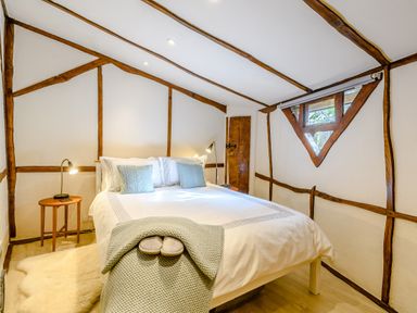 A bedroom with a bed pillows bedside tables lamps and a small triangular window at Brookbank Folly in Mitcheldean