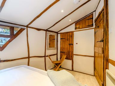 A bedroom with wooden beams white walls a wooden chair a wooden door and window at Brookbank Folly in Mitcheldean