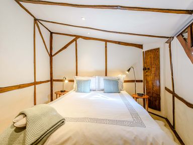 A bedroom with a bed two pillows two side tables with lamps and wooden beams on walls at Brookbank Folly in Mitcheldean