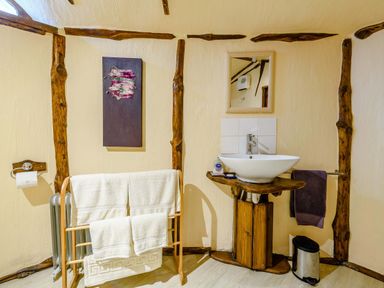 A bathroom with a wooden towel rack holding white towels a wall-mounted sink with a mirror above it a purple towel on a rail and a small silver trash bin at Brookbank Folly in Mitcheldean