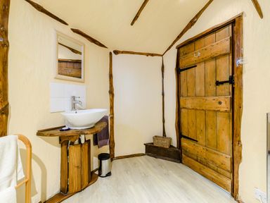 A bathroom with a wooden door a white sink on a wooden counter and a towel rack at Brookbank Folly in Mitcheldean