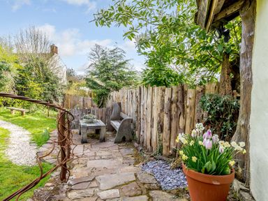 A garden seating area with a wooden bench and table next to a wooden fence with a potted plant of flowers nearby at Brookbank Folly in Mitcheldean
