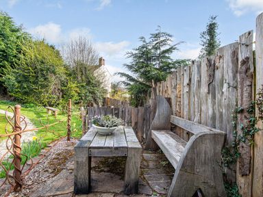 An outdoor seating area with a wooden bench and table with flowers surrounded by a wooden fence at Brookbank Folly in Mitcheldean