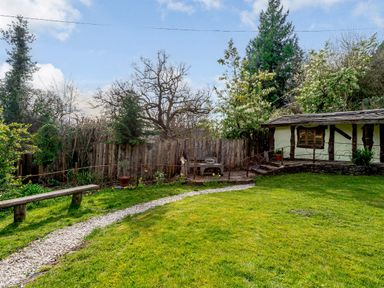 A garden with a gravel path wooden bench a small building and trees at Brookbank Folly in Mitcheldean