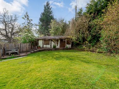 A grassy garden with a small wooden shed a wooden bench and trees and bushes at Brookbank Folly in Mitcheldean