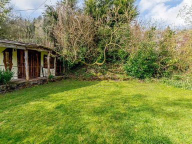 A grassy garden with leafless trees and shrubs next to a small rustic building at Brookbank Folly in Mitcheldean