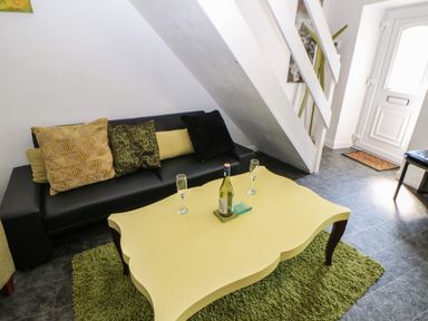 A living room with black sofa cushions and a yellow coffee table on a green rug next to a staircase and front door at Hollie Cottage in Haltwhistle