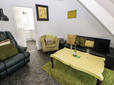 A living room with green armchair black sofa yellow coffee table and entrance to a kitchen at Hollie Cottage in Haltwhistle