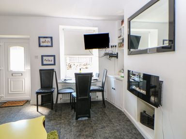 A dining area with a round table and four black chairs a wall-mounted TV and a fireplace at Hollie Cottage in Haltwhistle