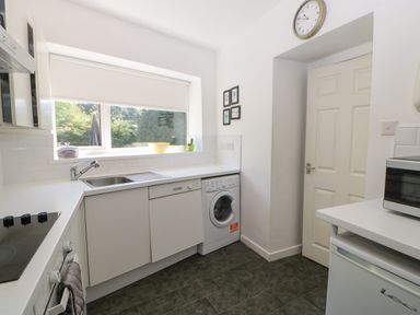 A kitchen with white cabinets a washing machine a sink a stove a microwave and a window at Hollie Cottage in Haltwhistle