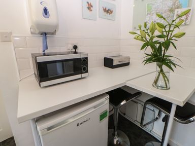 A kitchen corner with a microwave on the counter a mini fridge a vase with flowers two bar stools and some wall decorations at Hollie Cottage in Haltwhistle