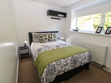 A bedroom with a bed a bedside table lamps a window with a blind and pictures on the sill at Hollie Cottage in Haltwhistle